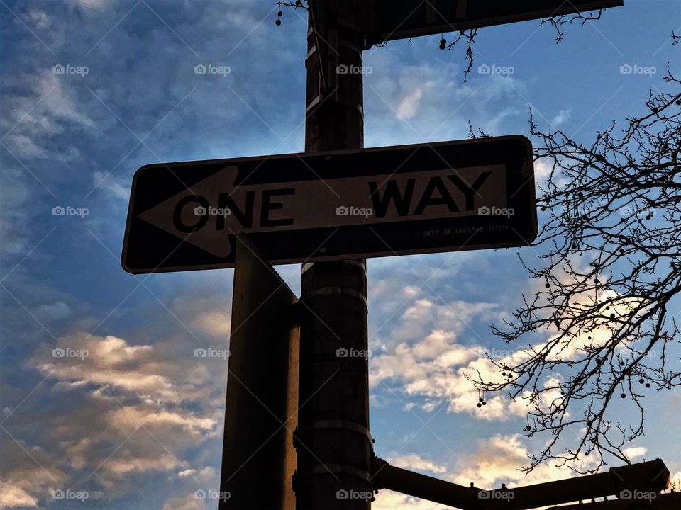 A photo of a “one way” sign against a beautiful sky with glowing clouds.