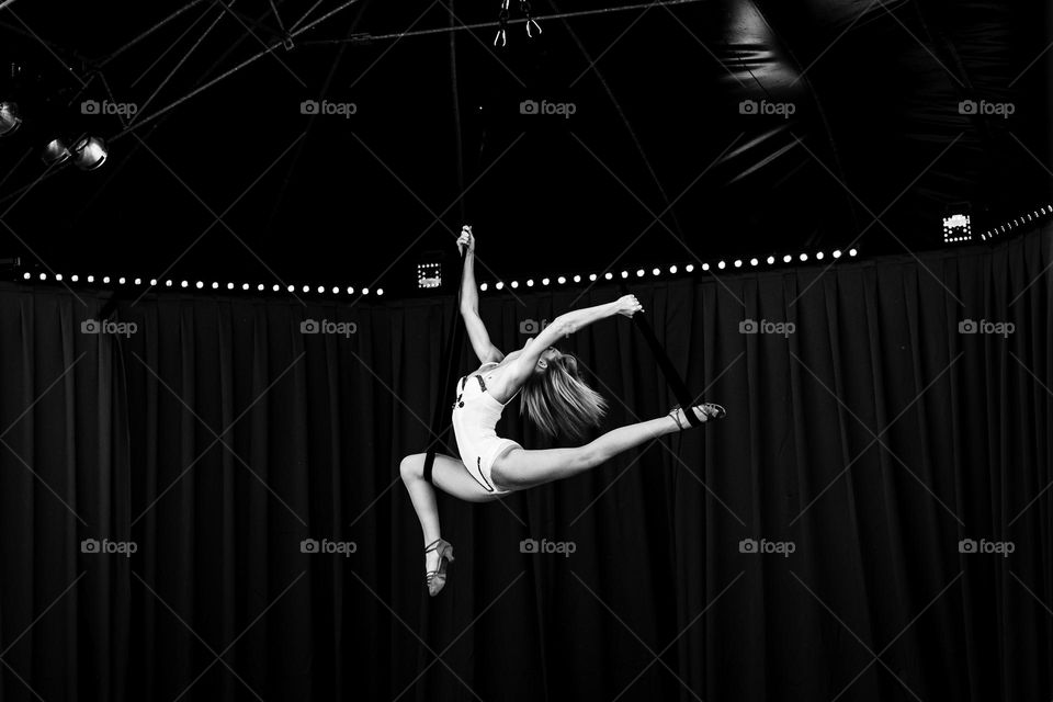 a black and white Portrait of a gracious pose of a professional circus entertainer performing a fantastic act on ropes above the arena of a circus tent