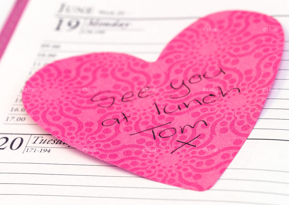 A pink heart shaped note with a message on an open page in a diary.