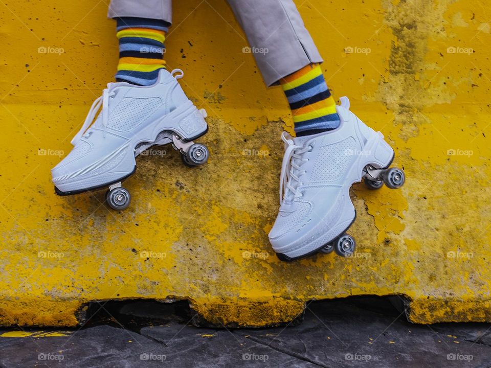 Close-up of shoe skates against yellow painted concrete barrier wall