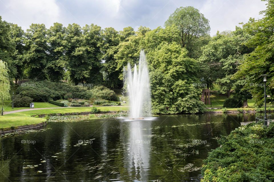 Beautiful fountain in the middle of a pond surrounded by green grass and trees in a park of Boras city Sweden 