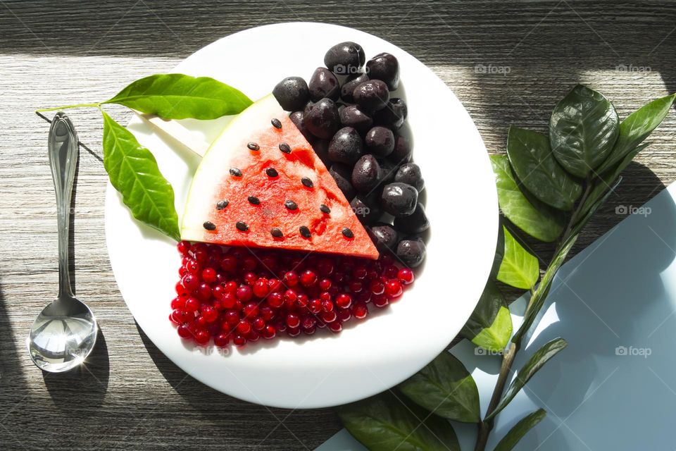 Fresh and healthy fruits and berries lie on a white plate on a wooden background.