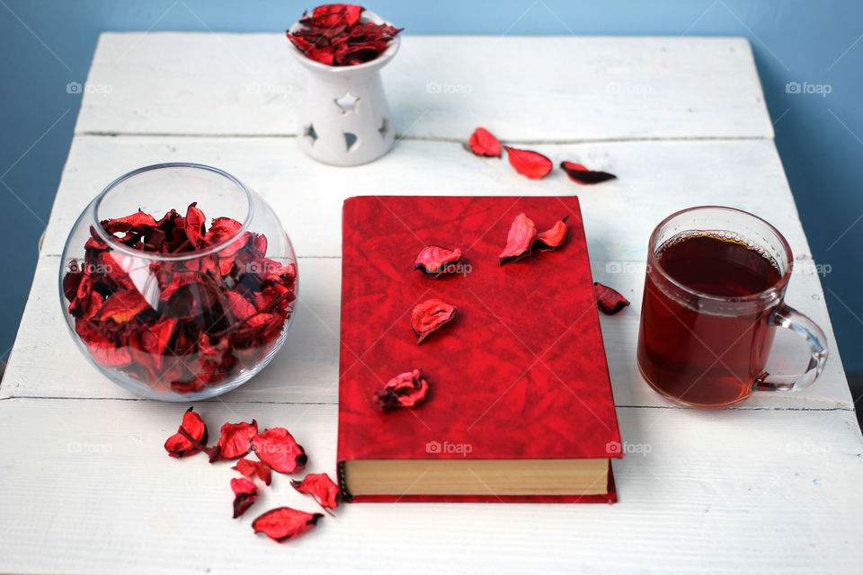 Cup of tea with a book and a vase of rose petals on the dazzling white table