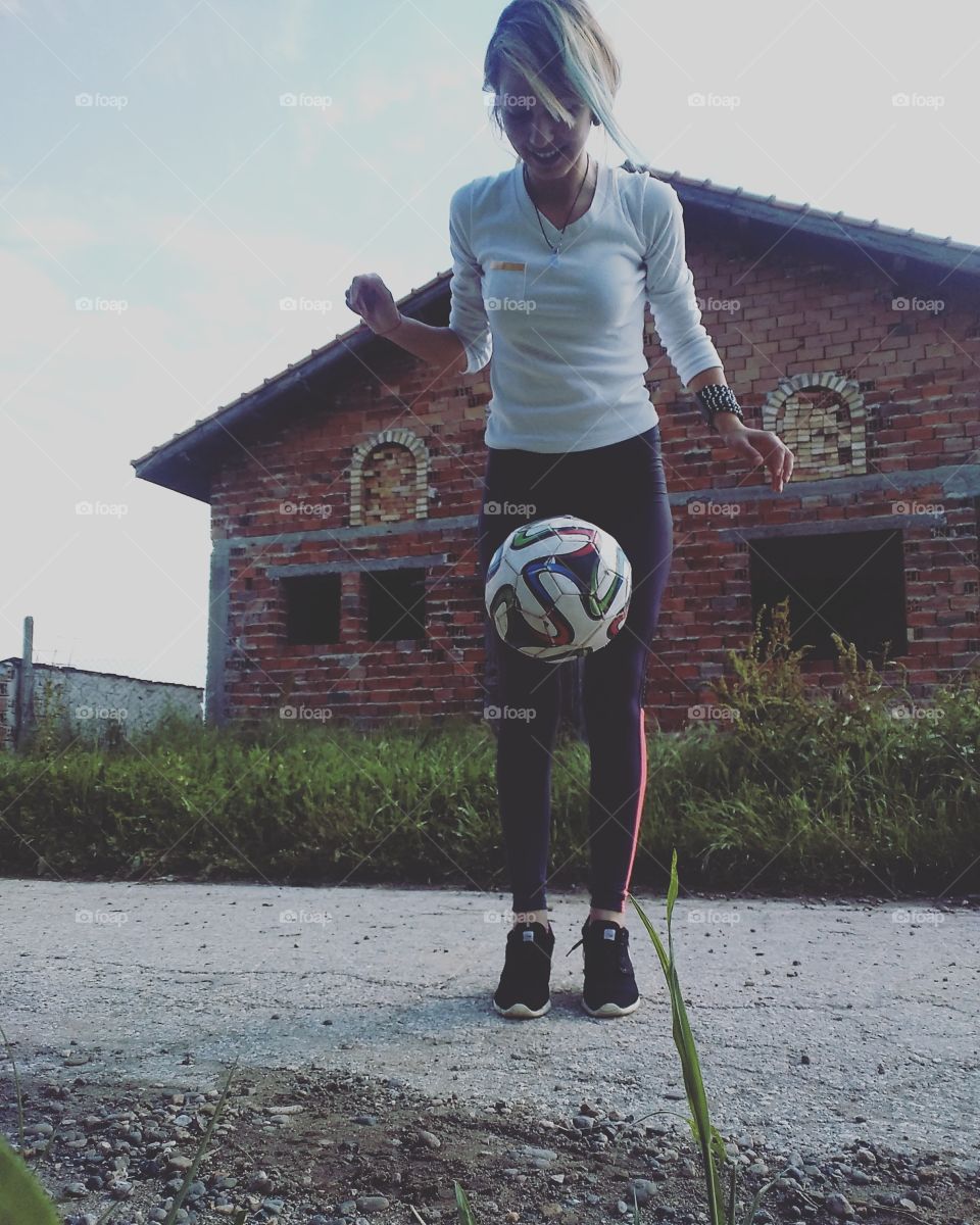 Young woman playing with football in front of house