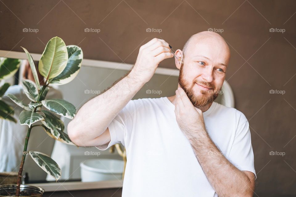 Adult handsome man with pipette with beard oil in bathroom at home