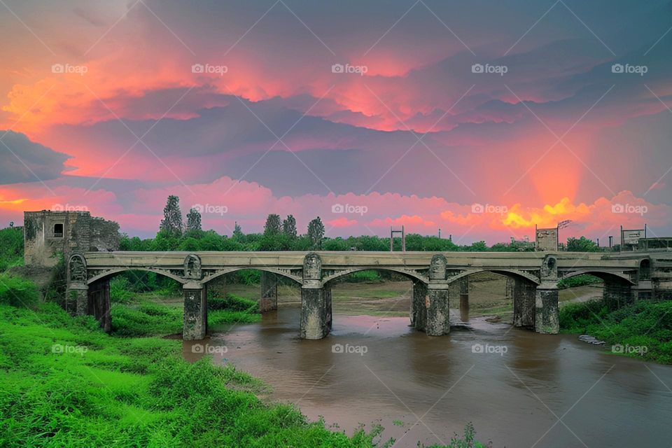 Old abandoned bridge spanning river with sun setting in background