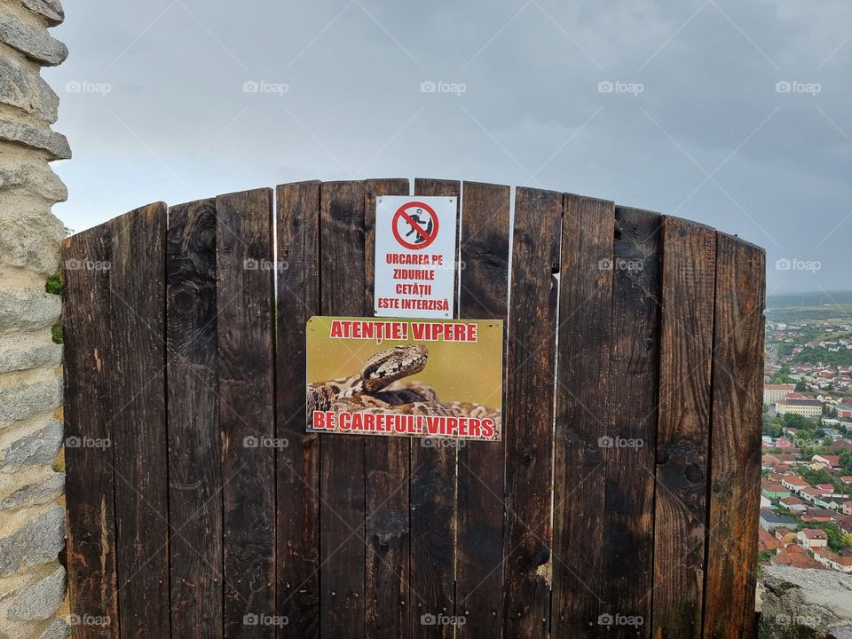 Wooden fence with warning signs: warning against vipers and warning for risk of falling