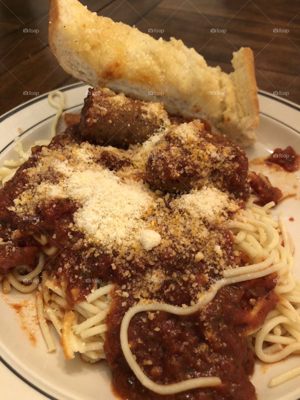 Spaghetti and meatballs and cheese with garlic bread displayed  on a plate. 