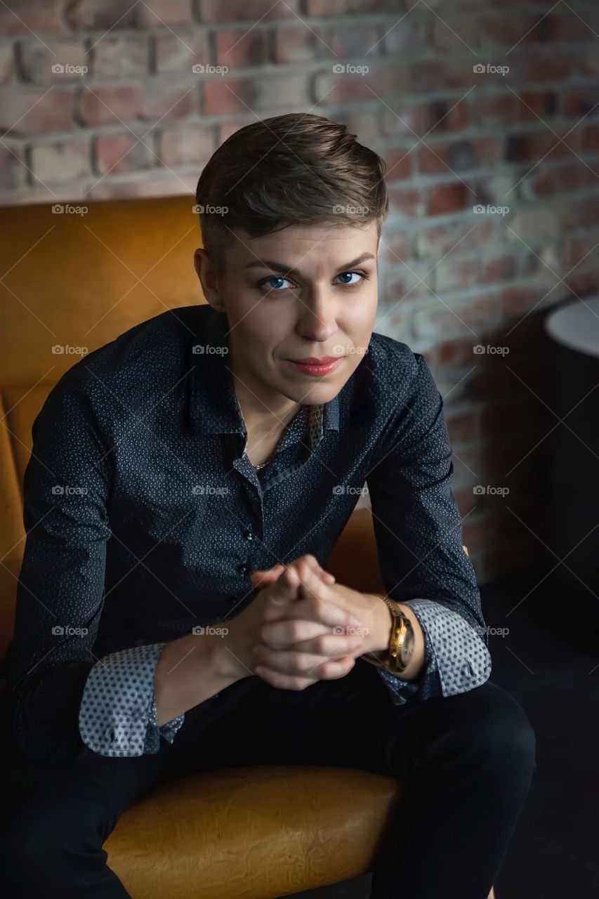 A business woman with a short haircut sits on a yellow armchair, a beautiful portrait with a look at the camera, beautiful eyes