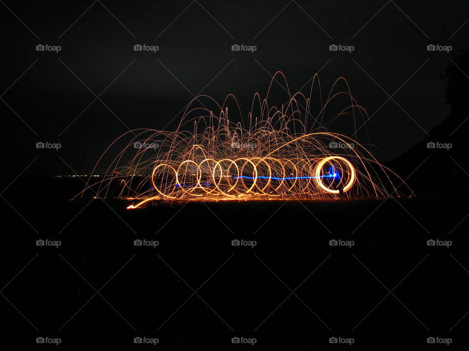 Circles of sparks flying from steel wall with the blue line in the middle of the night beach