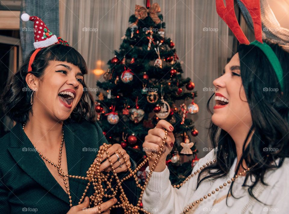 Two happy women having fun while decorating a christmas tree