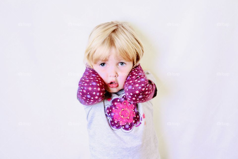 Sweet little girl holding her head with stark white background behind her in this cute pose. 