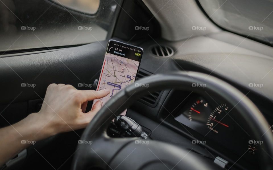 The hand of a young Caucasian unrecognizable male driver is dialing a route using a mobile phone on the front of the car, close-up side view. Road trip concept.