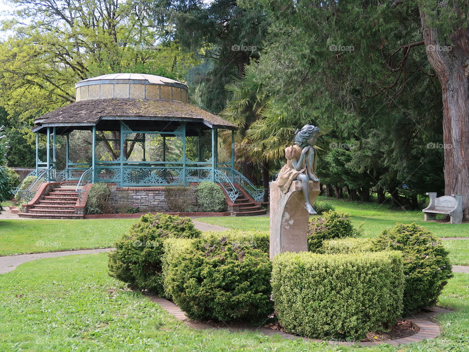A nice little landscaped park with a modern gazebo and a beautiful stone statue. 