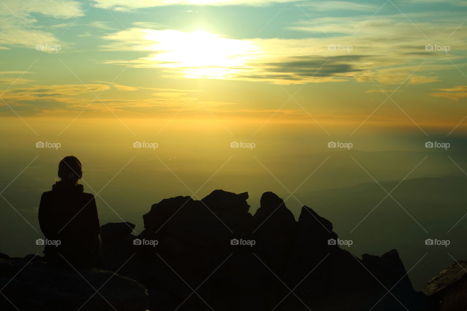 silouette at sunset. woman relaxing sitting on rocks looking landscape