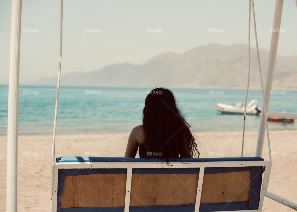 Brunette girl sit at swing with beautiful sea view 