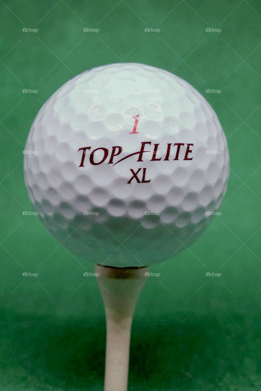 Top Flite 1 XL golf ball on wooden tee with green backdrop.