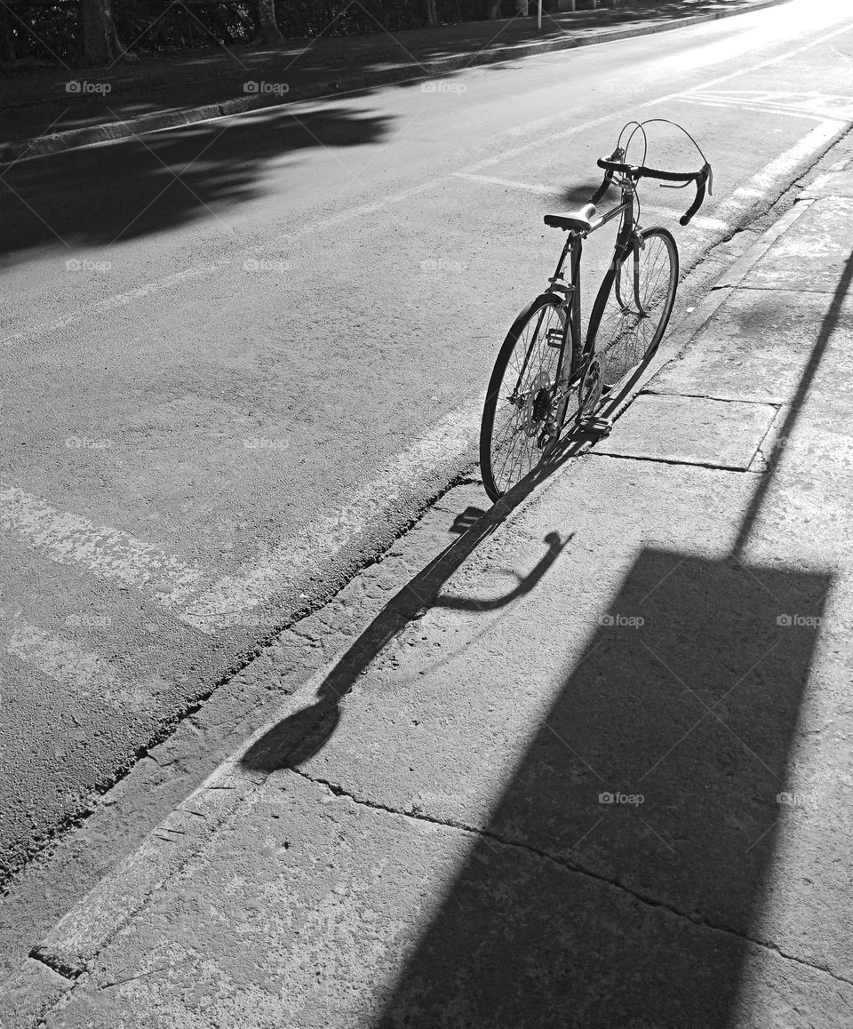 And old bycicle on the street between a sidewalk and the street, shadows of a sign and the bycicle