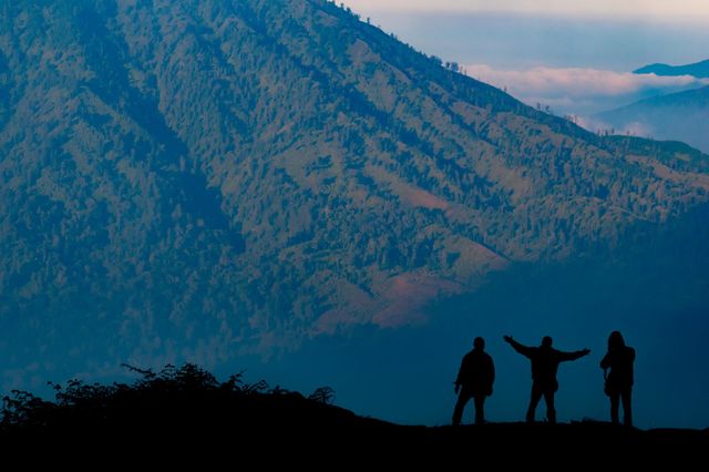 silhouette of three people stopping by the enjoy the view of a mountain, a short break before continue to walk to reach the mountain