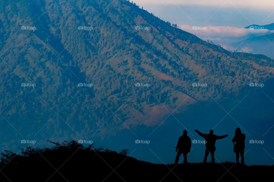 silhouette of three people stopping by the enjoy the view of a mountain, a short break before continue to walk to reach the mountain