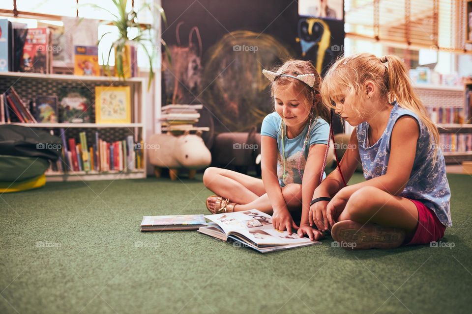 Two primary schoolgirls doing homework in school library. Students learning from books. Pupils having fun in library. Back to school