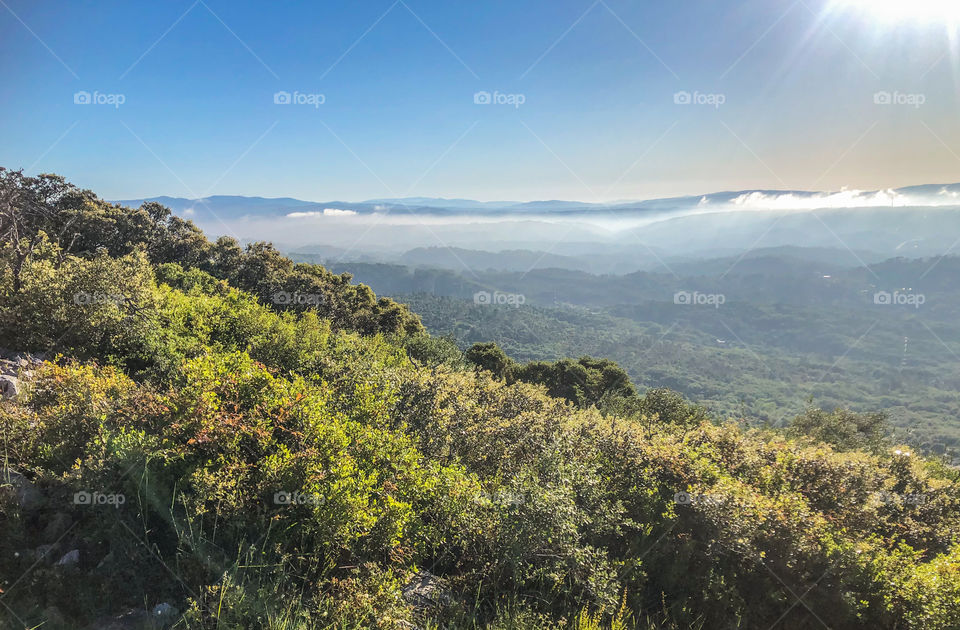 Sun shines down on a green landscape with cloud covered mountains in the distance