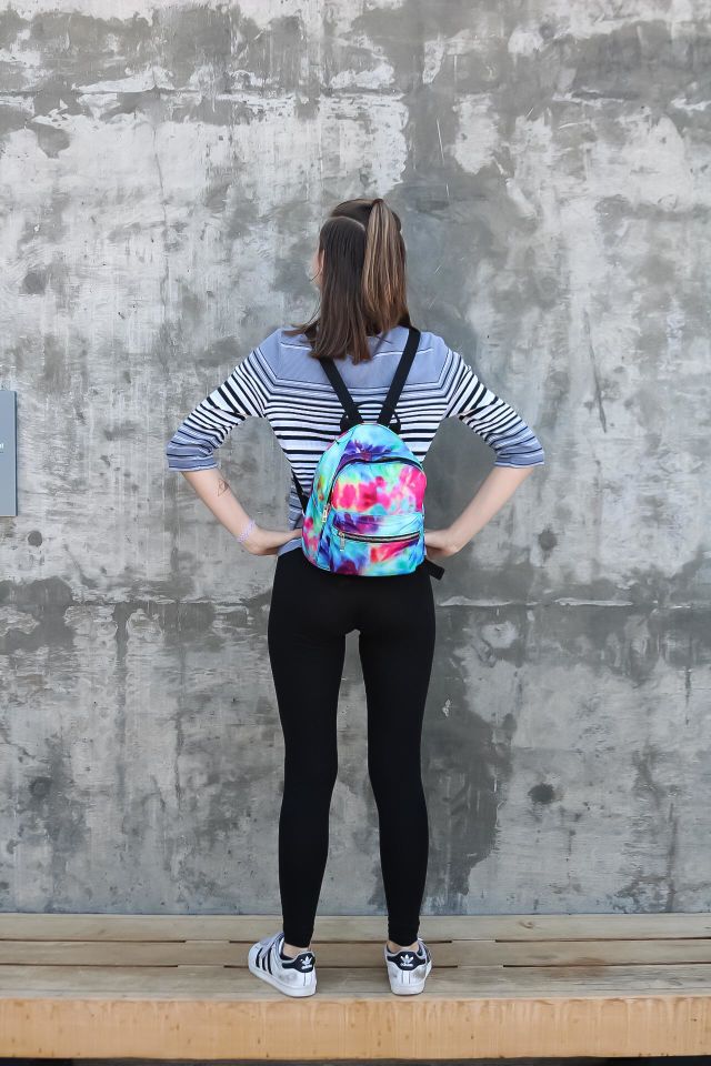 Striking a pose in front of a cement wall with a tie dye style backpack ready to explore the world 