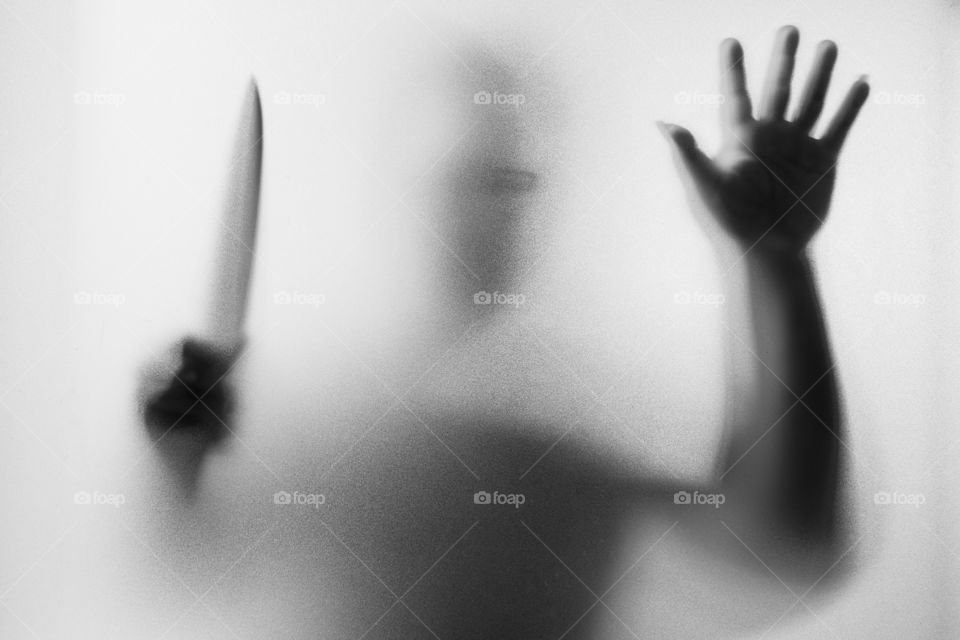 Horror Murderer. Dangerous man behind the frosted glass with a knife on his hand.Halloween background.Black and white picture