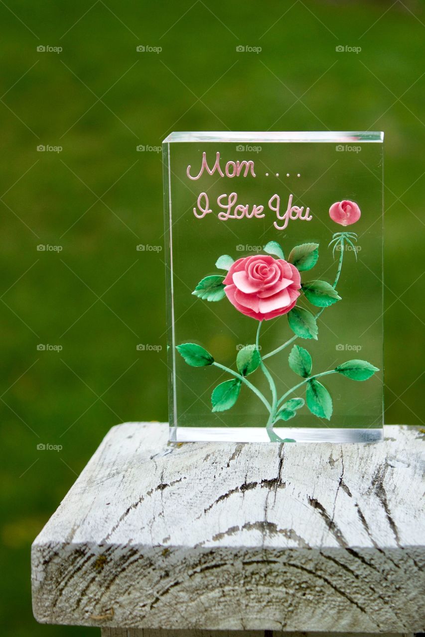 “Mom....I Love You” plaque outdoors on a weathered white post against a blurred grass background  (portrait)