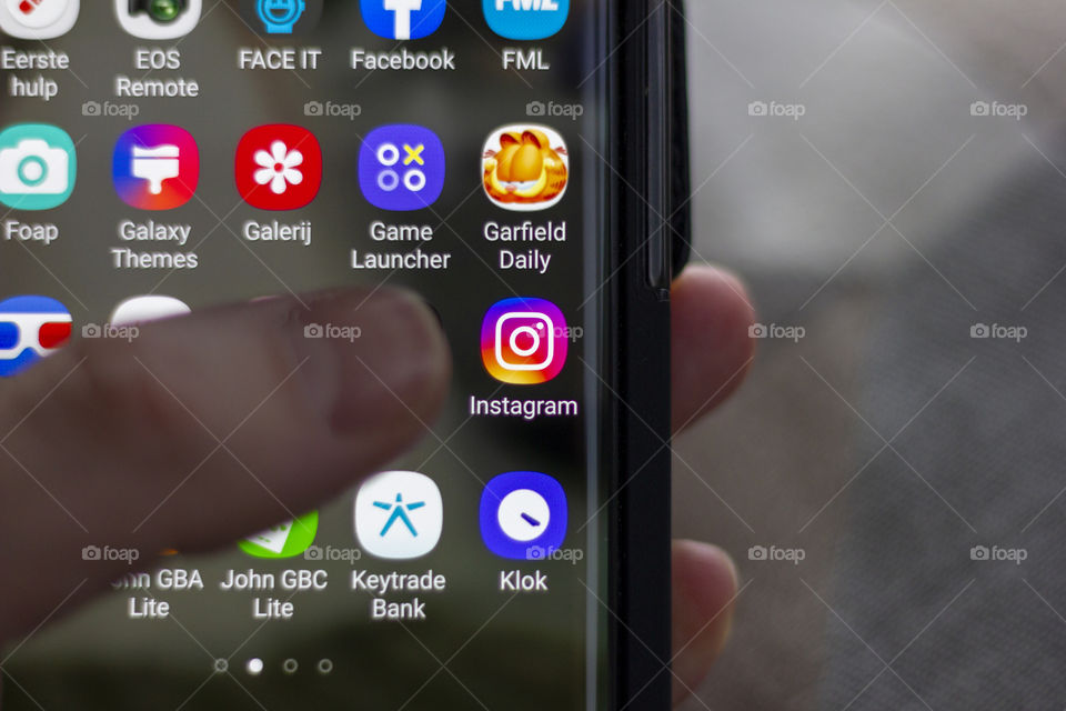 A close up portrait of a smartphone held by a hand. the thumb of the user is ready to start the in focus application Instagram. social media is a daily habit for a lot of people.