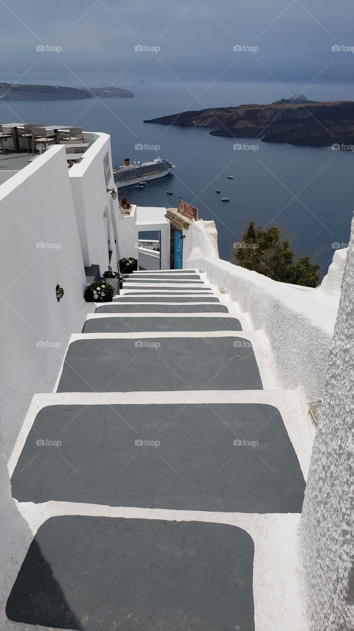 view from up high in Santorini, Greece, looking down a steep staircase towards the ocean and cruise ship