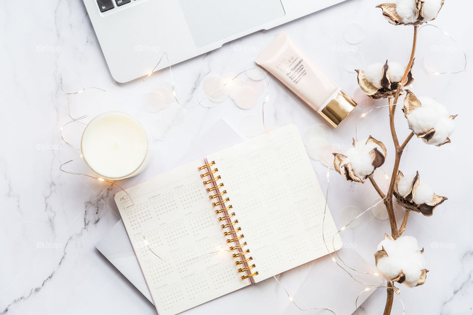 Desktop flatlay items: laptop, calendar, candle, garland, cotton flowers lying on marble background 