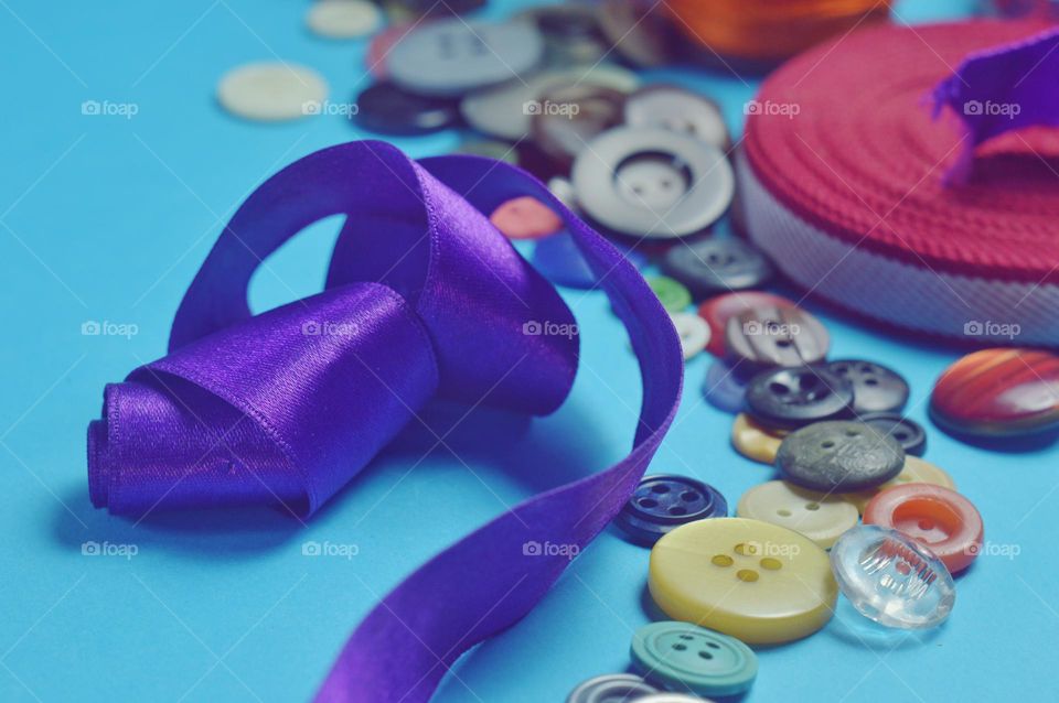 a beautiful purple ribbon and a lot of multi-colored buttons lie on a blue background