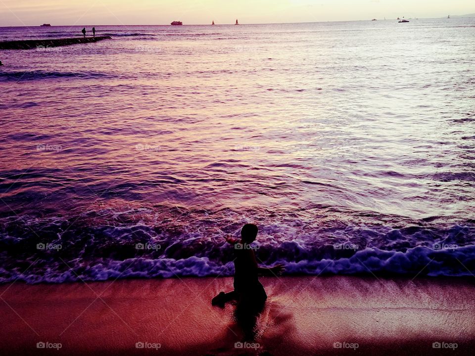boy plays in the surf line as the sun sets over Waikiki Beach