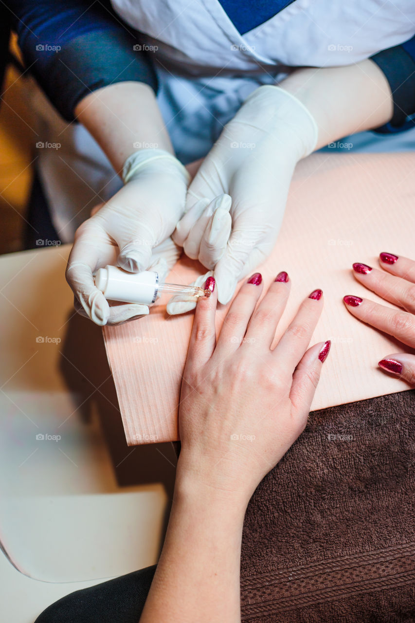 Beautician in a beauty salon doing a hybrid manicure. Painting and styling nails. Woman getting professional nails treatment. Close up of hands