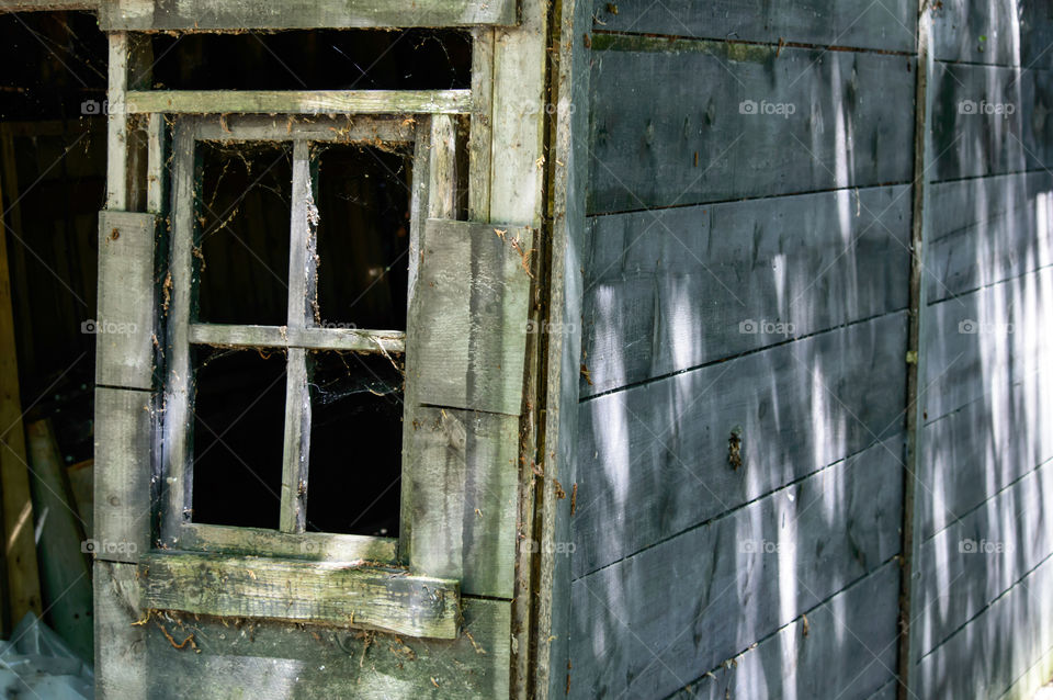 Side angle view of old wood frame building with window missing glass and rustic wood frame with boards deteriorating over time 