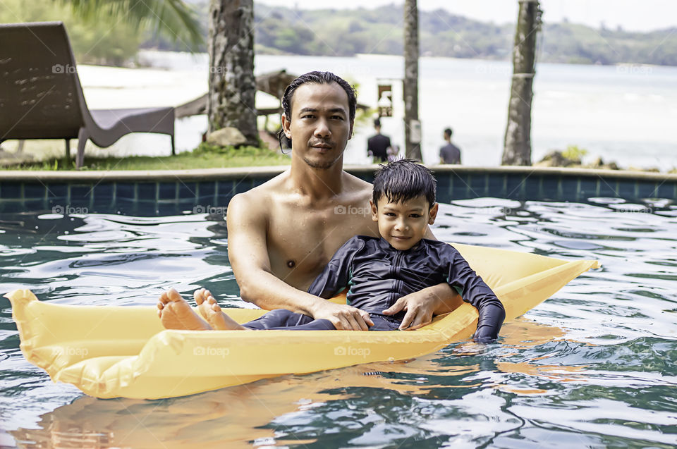 Portrait of a father and son in swimming pool background sea and coconut trees.