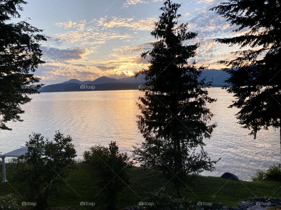 Summer sunset on the banks of Lake Pend Oreille near Sand Point, Idaho with tall pines in foreground and mountains in the background 