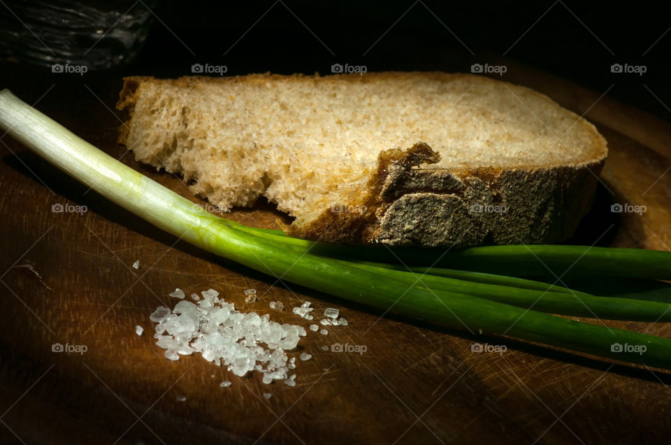 Slices of rye bread served with green onion and coarse salt on wooden cutting board light brush technique