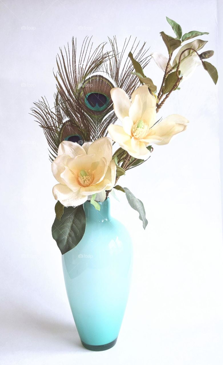 high key still life blue glass vase with flowers and peacock feathers  in front of a white background