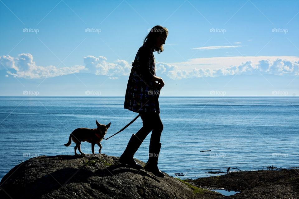 Girl and her dog walking on a scenic hill overlooking the Pacific Ocean - silhouette and shadow