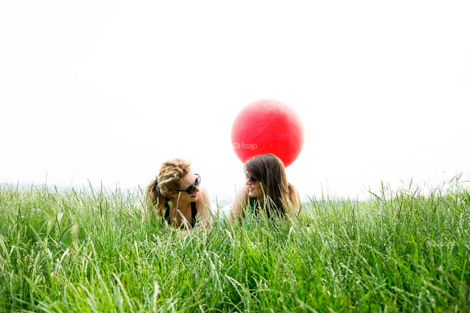 two girls lying in the grass. two young girls best friends lying in the grass with big red balloon behind them