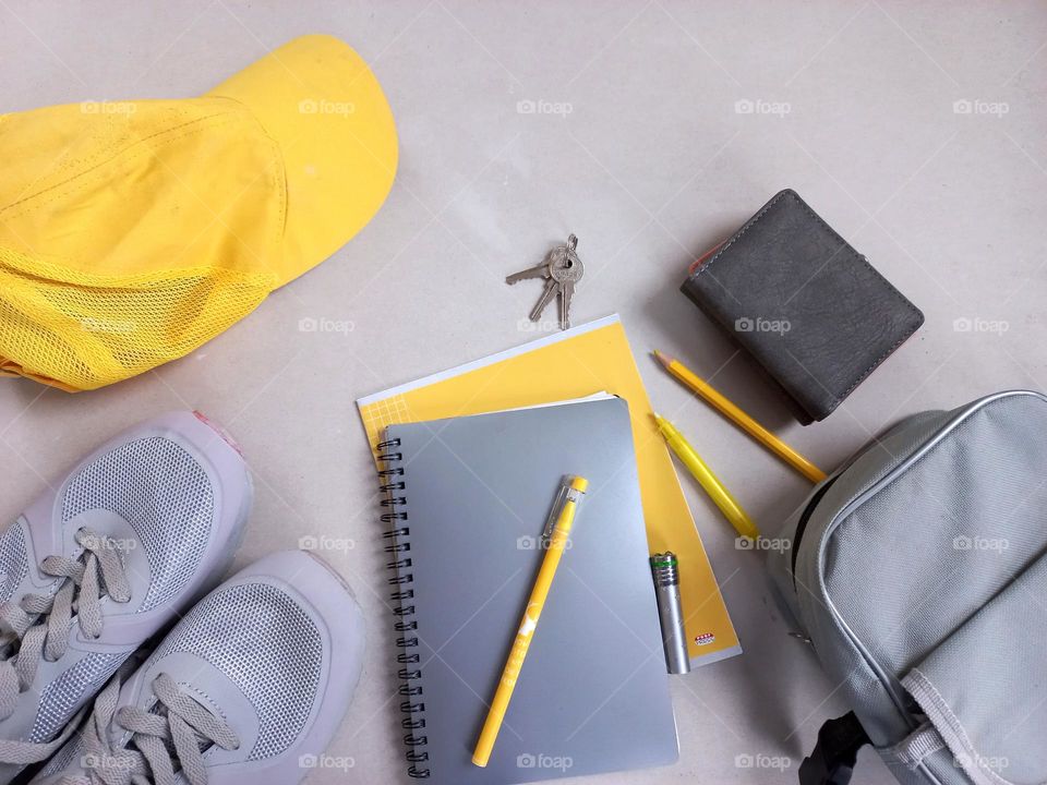 items and accessories in yellow-gray colors, these are gray sneakers, a gray bag, a gray wallet, a gray notebook and a yellow cap, a yellow notebook, a pen, a pencil.
