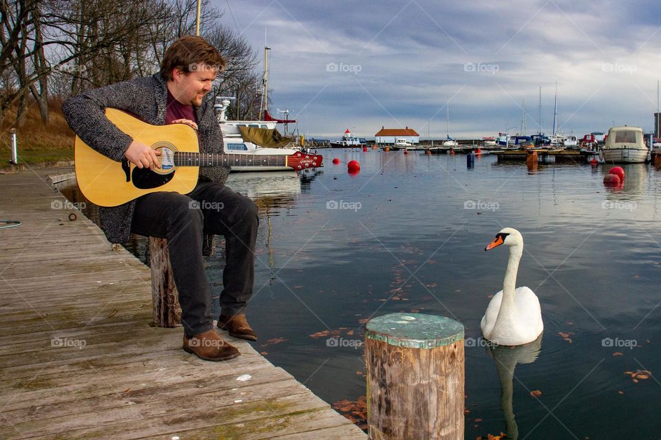 The musican and the Swan.
this photography tells a different story .
the man was sitting at the pir and playing a spring day ,suddenly this Swan shows up and was floating around him and just listen