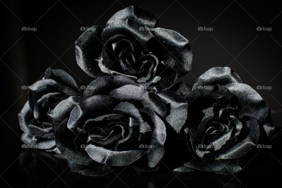 Dark low key photo of 4 black fabric roses on a dark background 