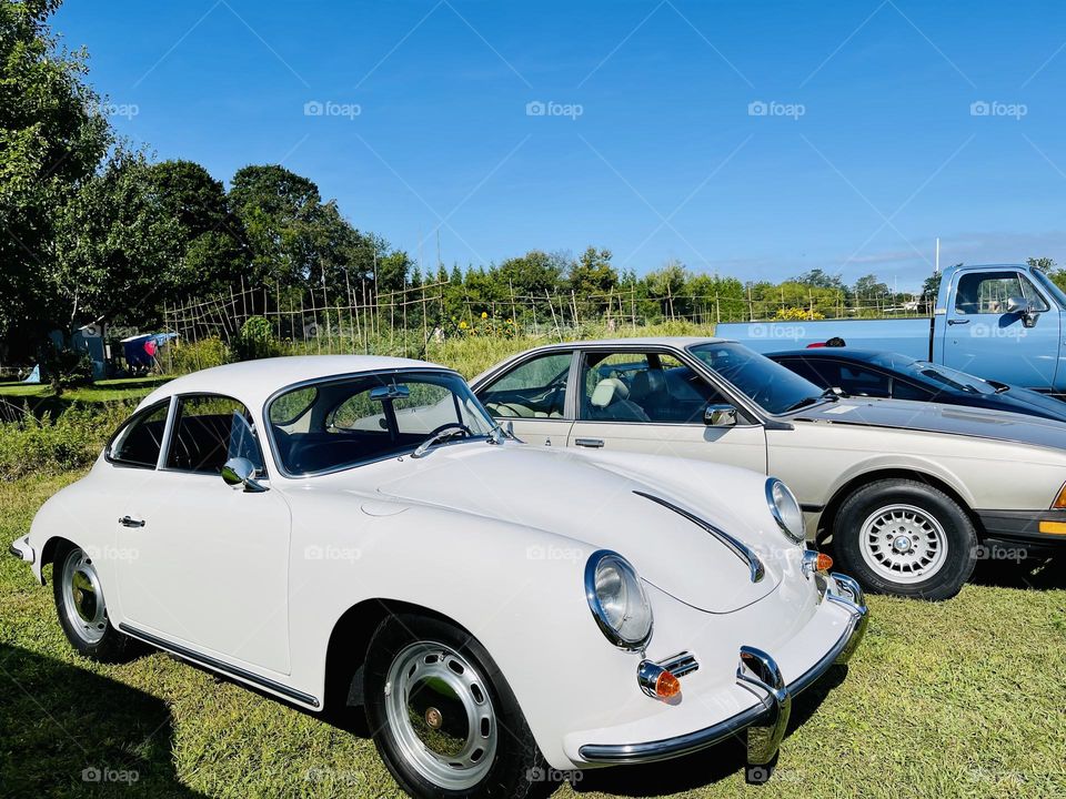 White sports car on display. Sleek and beautiful against sunny blue sky and a lush green field.