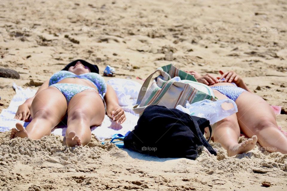 Two friends sunbathing on the beach and laughing together 