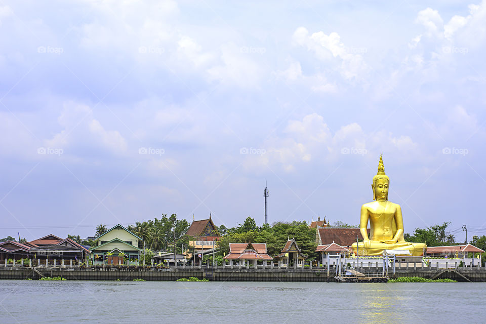 Big Buddha golden and the house behind Chao Phraya River. Background sky and clouds at Wat Bang Chak in Nonthaburi , Thailand.