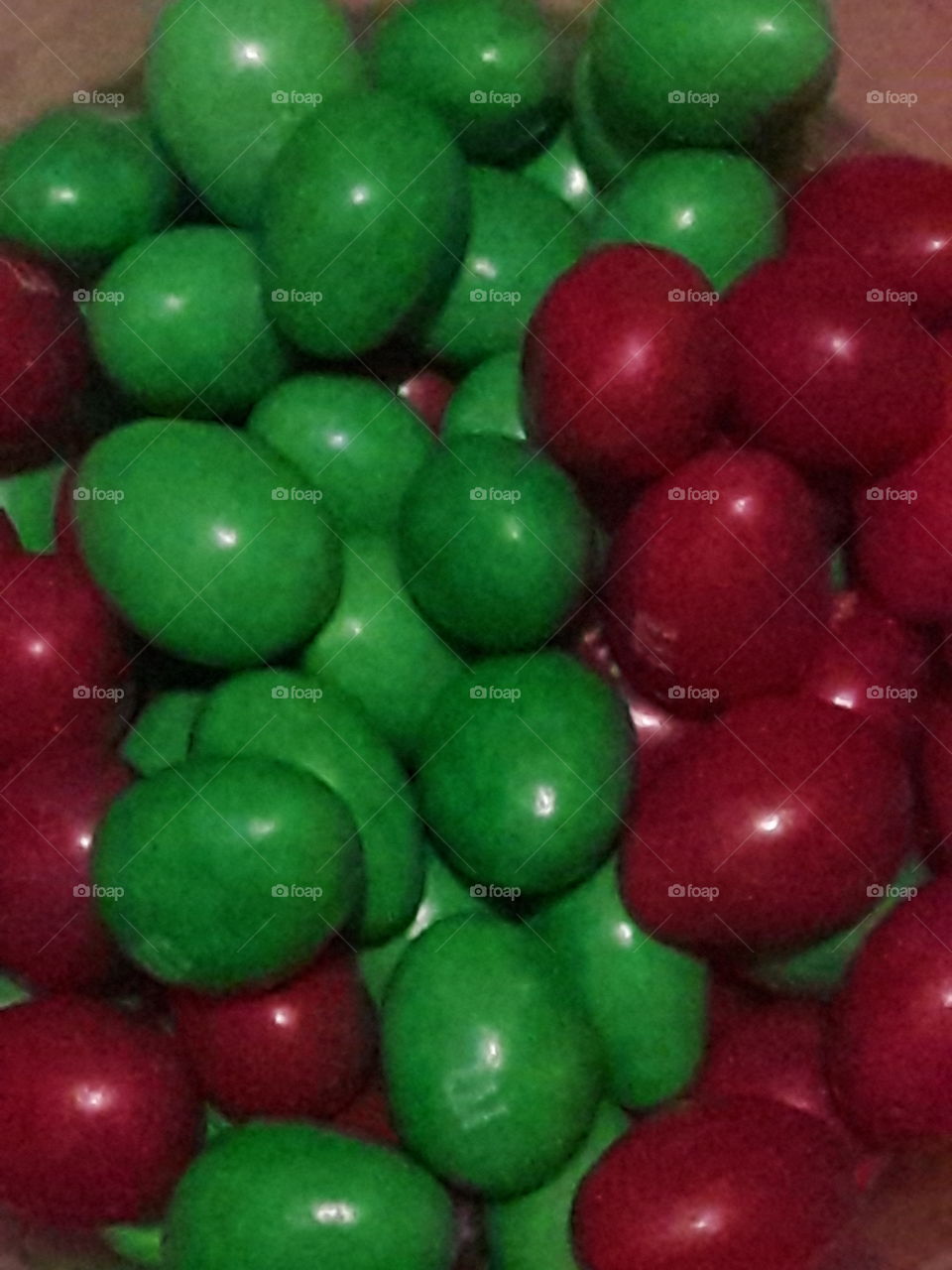 A close up of a bunch of green and red chocolate coated  candy in a bowl.