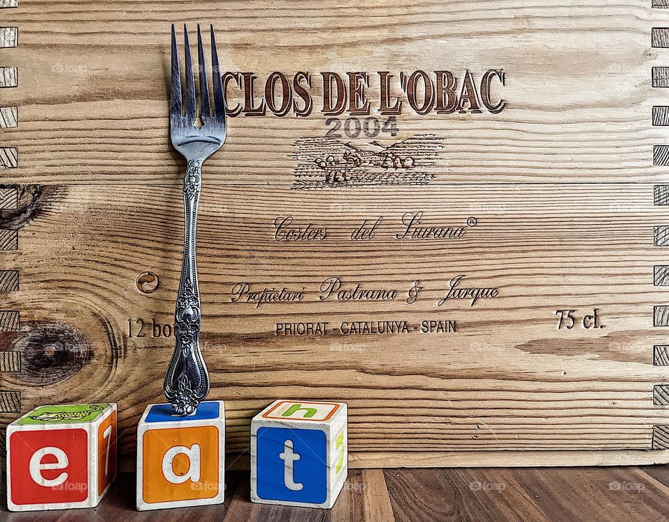 Fork with the word eat spelled out in blocks and a background of a wine box, unique interpretation of a fork, not ordinary fork photograph, different forks, wooden blocks spelling out words, wooden wine box for a background